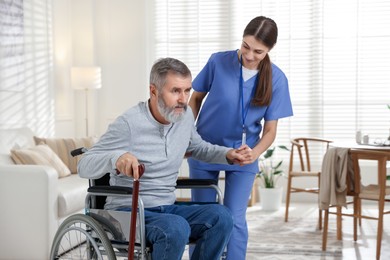 Photo of Caregiver assisting senior man in wheelchair indoors. Home health care service