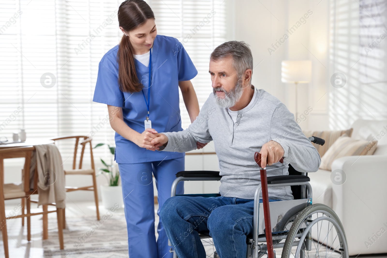 Photo of Caregiver assisting senior man in wheelchair indoors. Home health care service