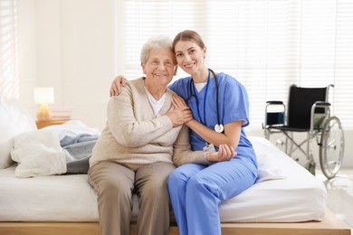 Photo of Caregiver supporting senior woman on bed indoors. Home health care service