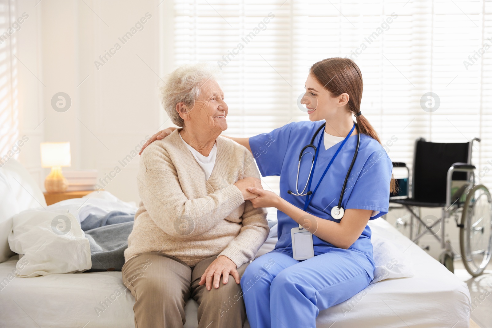 Photo of Caregiver supporting senior woman on bed indoors. Home health care service