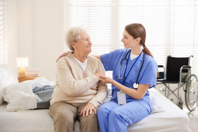 Photo of Caregiver supporting senior woman on bed indoors. Home health care service