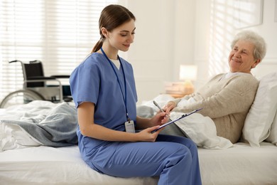 Photo of Caregiver examining senior woman on bed indoors. Home health care service