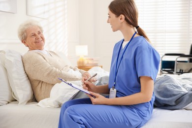 Caregiver examining senior woman on bed indoors. Home health care service