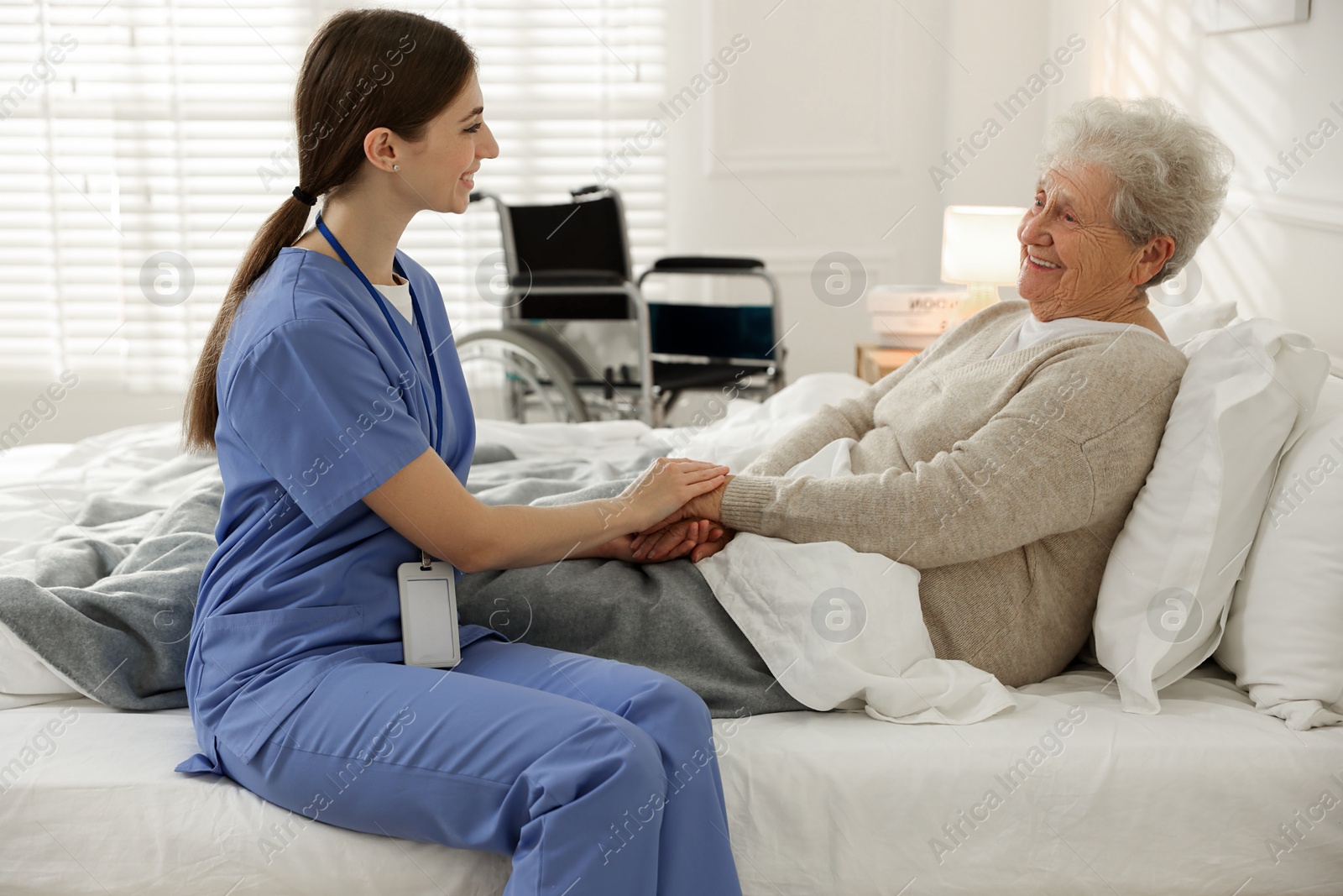 Photo of Caregiver supporting senior woman on bed indoors. Home health care service