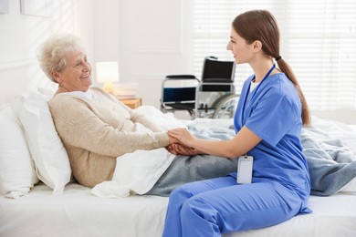 Caregiver supporting senior woman on bed indoors. Home health care service