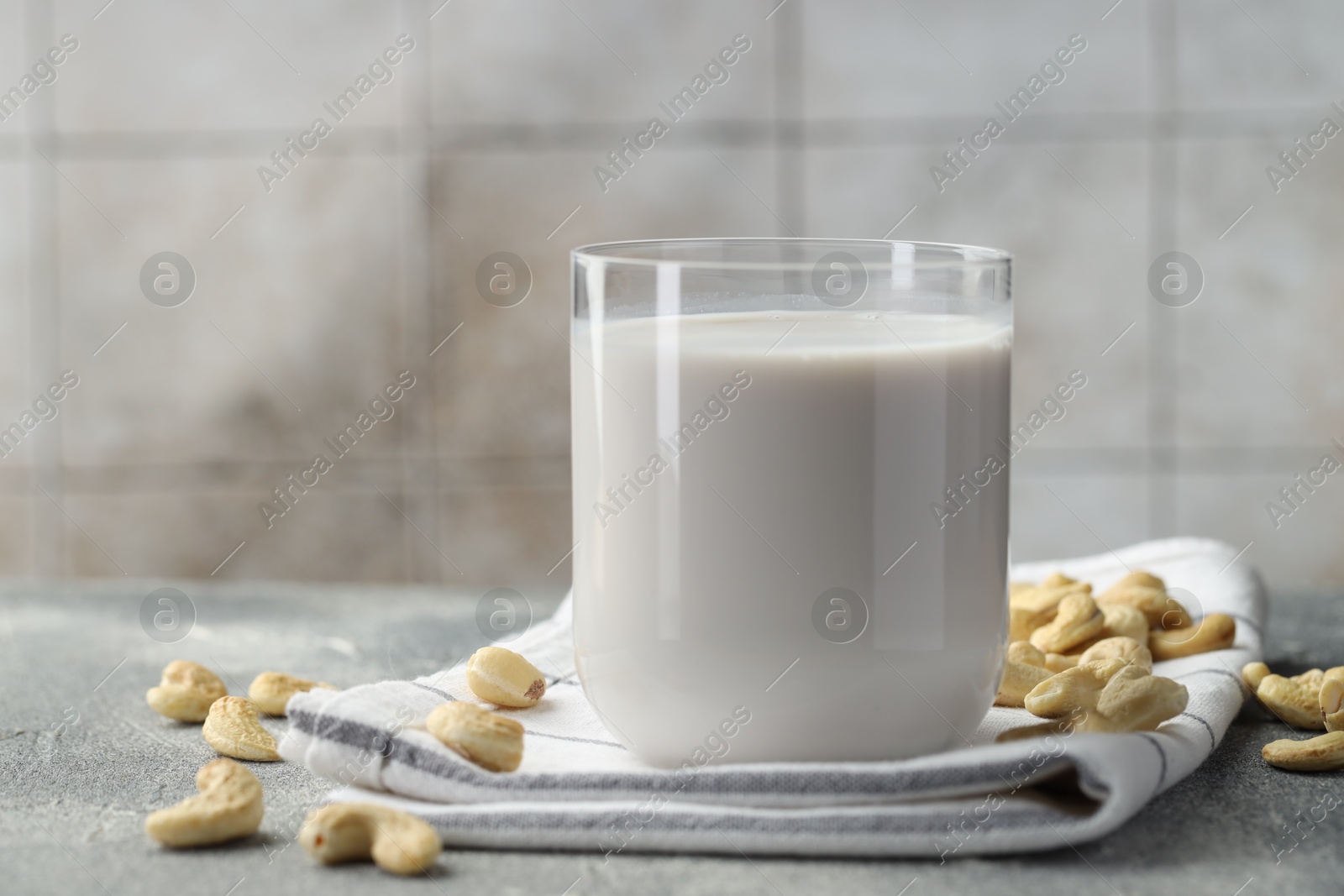 Photo of Fresh cashew milk in glass and nuts on grey textured table, closeup