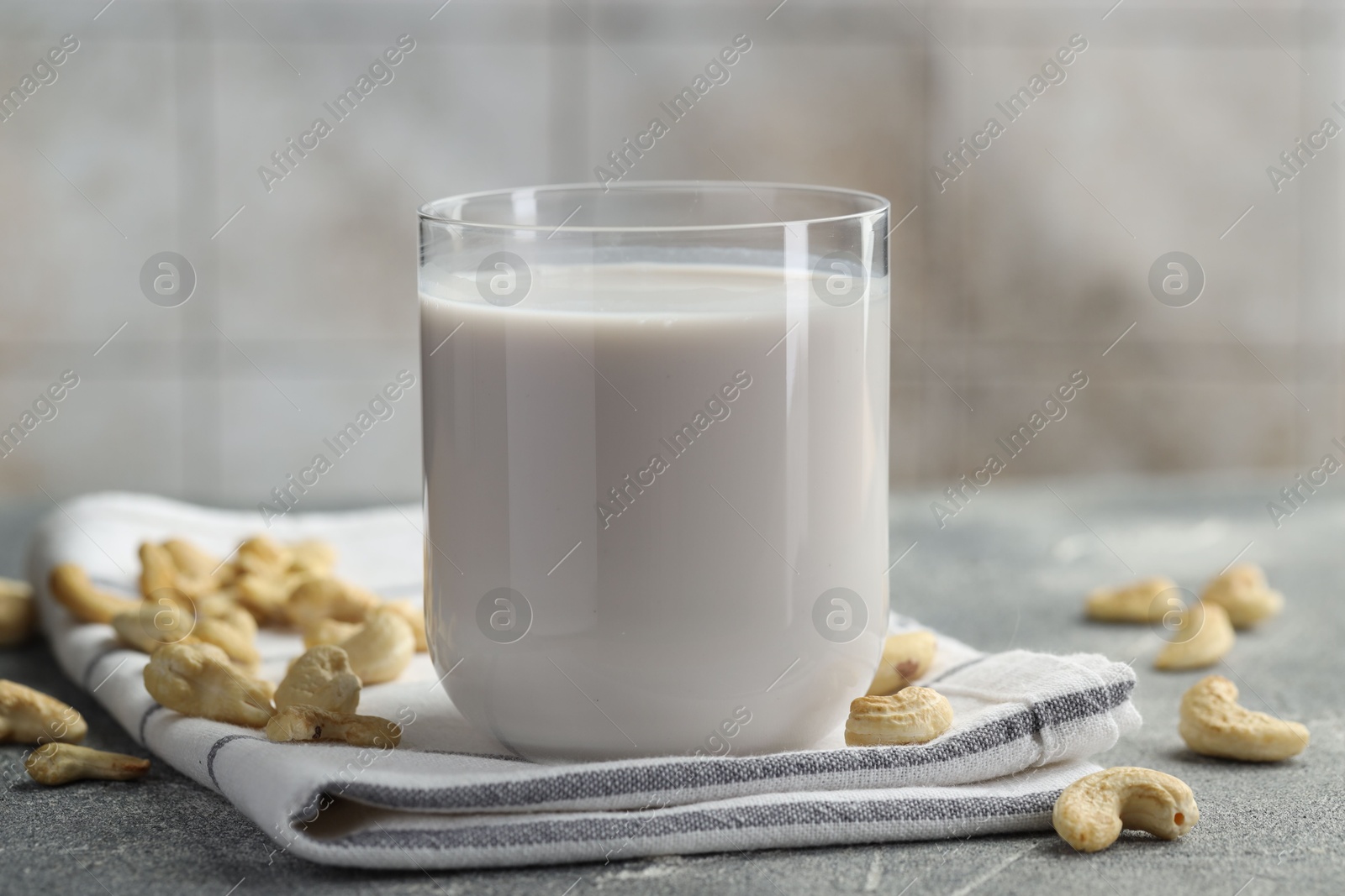 Photo of Fresh cashew milk in glass and nuts on grey textured table, closeup