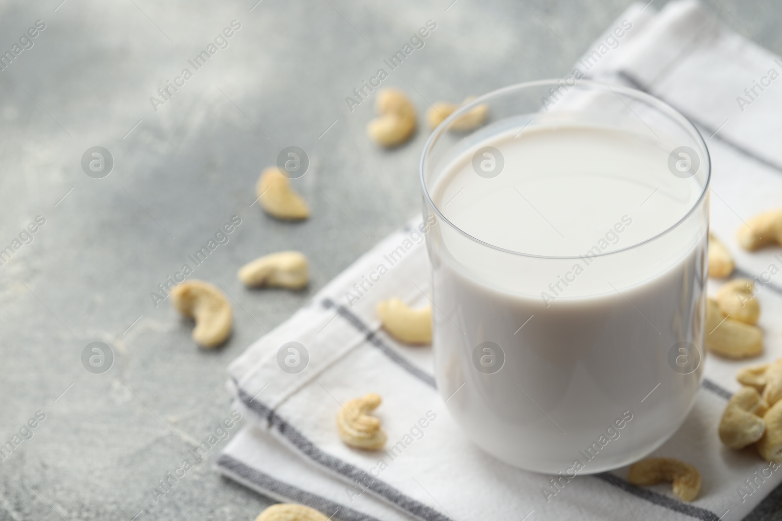 Photo of Fresh cashew milk in glass and nuts on grey table, closeup. Space for text