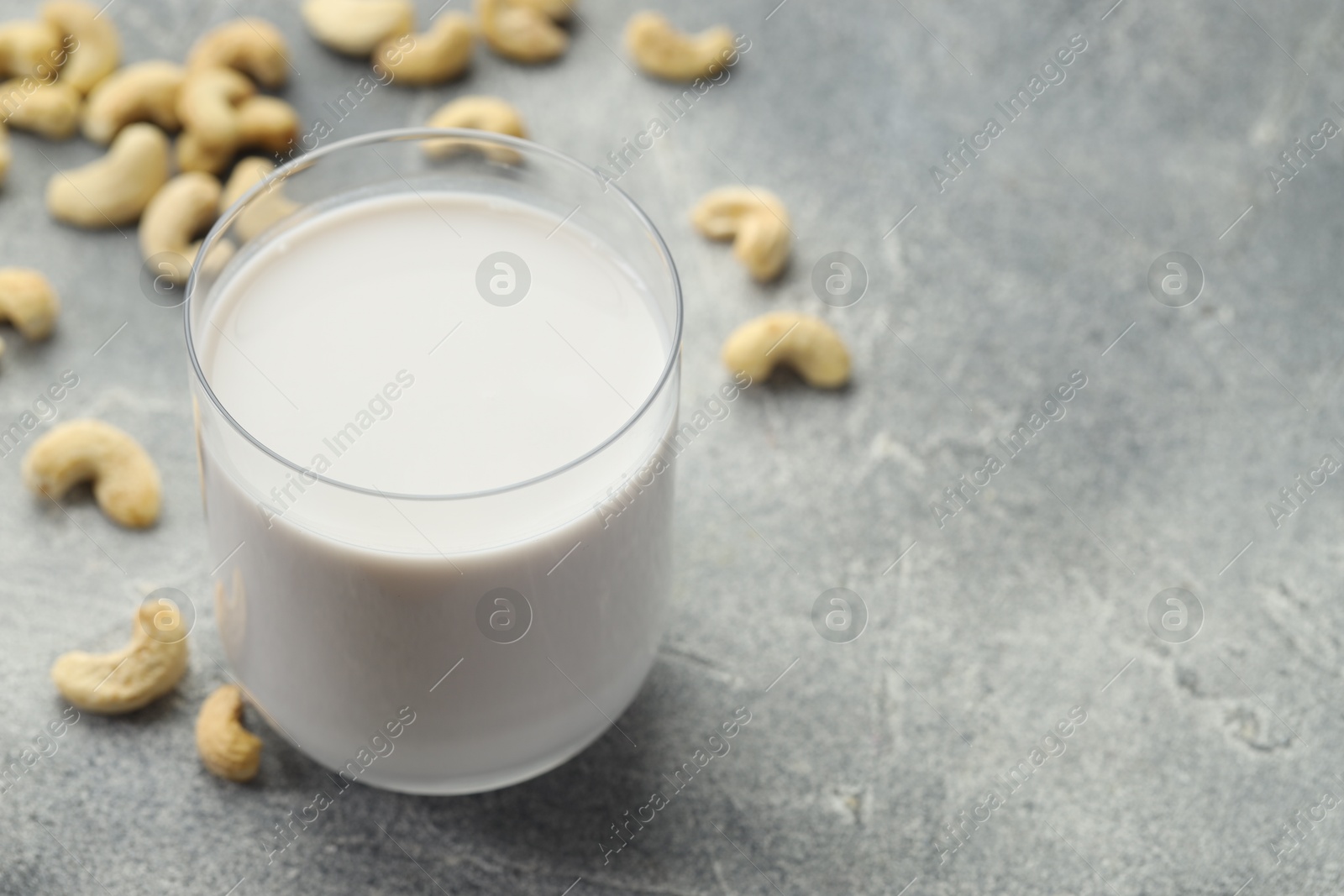 Photo of Fresh cashew milk in glass and nuts on grey table, closeup. Space for text