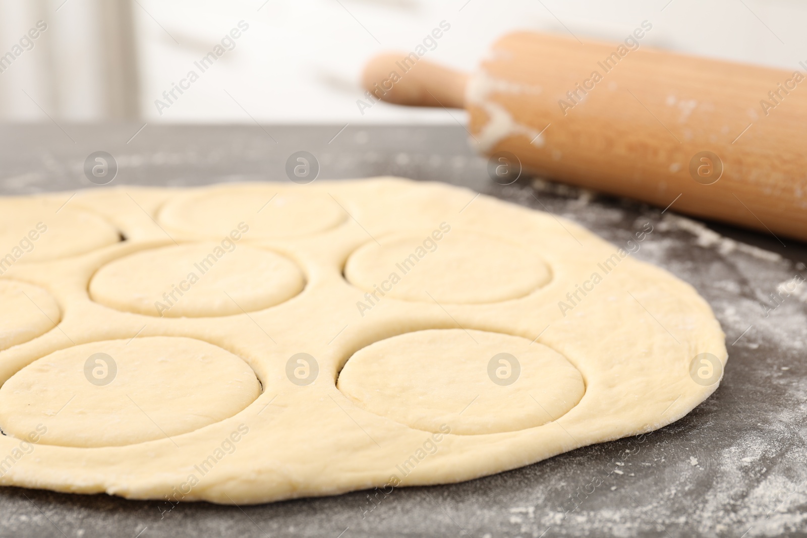 Photo of Making pirozhki (stuffed pastry pies). Raw dough and rolling pin on gray table, closeup