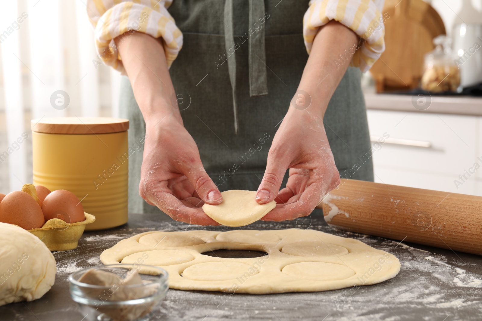 Photo of Woman making pirozhki (stuffed pastry pies) at gray table indoors, closeup