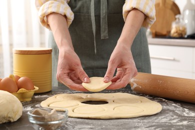 Photo of Woman making pirozhki (stuffed pastry pies) at gray table indoors, closeup