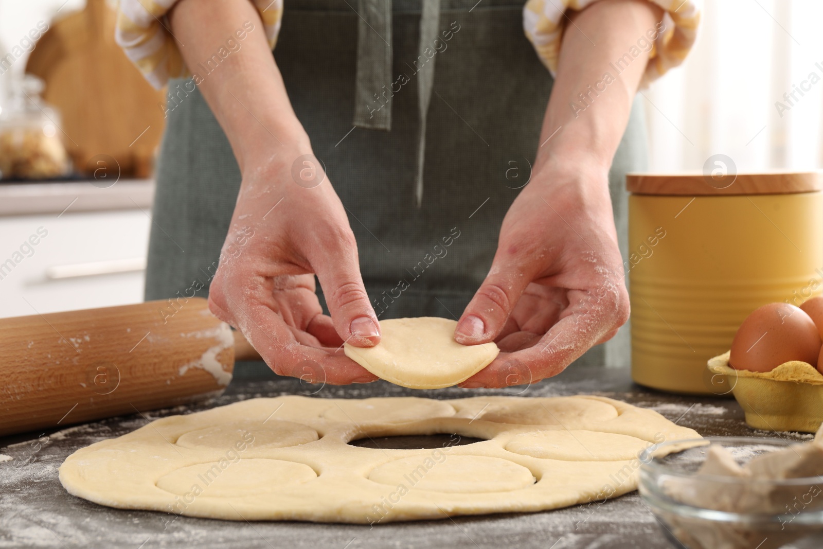 Photo of Woman making pirozhki (stuffed pastry pies) at gray table indoors, closeup