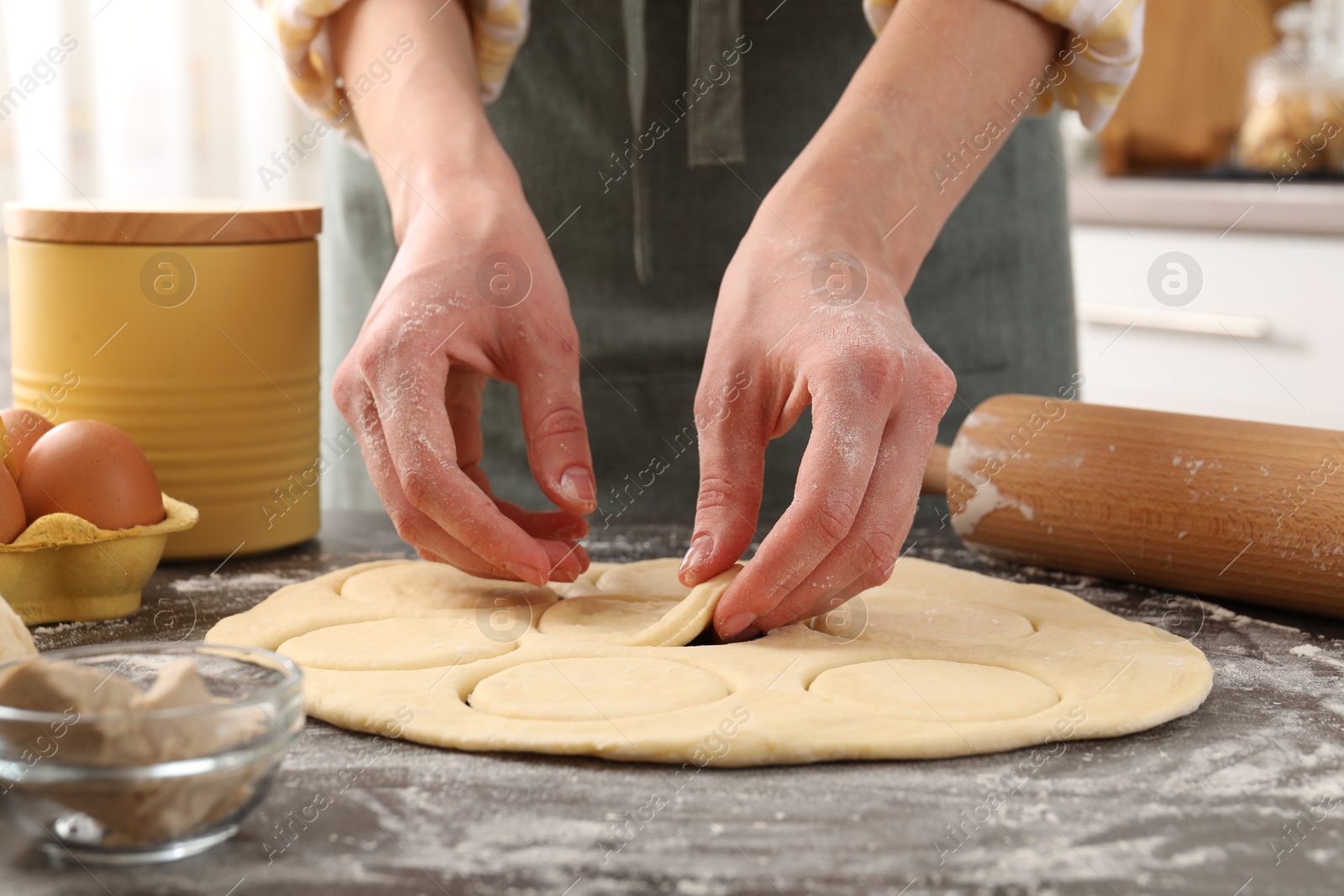 Photo of Woman making pirozhki (stuffed pastry pies) at gray table indoors, closeup