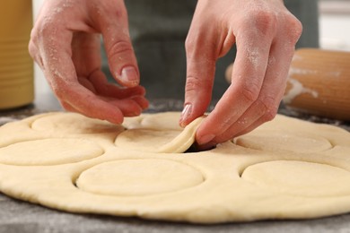 Photo of Woman making pirozhki (stuffed pastry pies) at gray table indoors, closeup