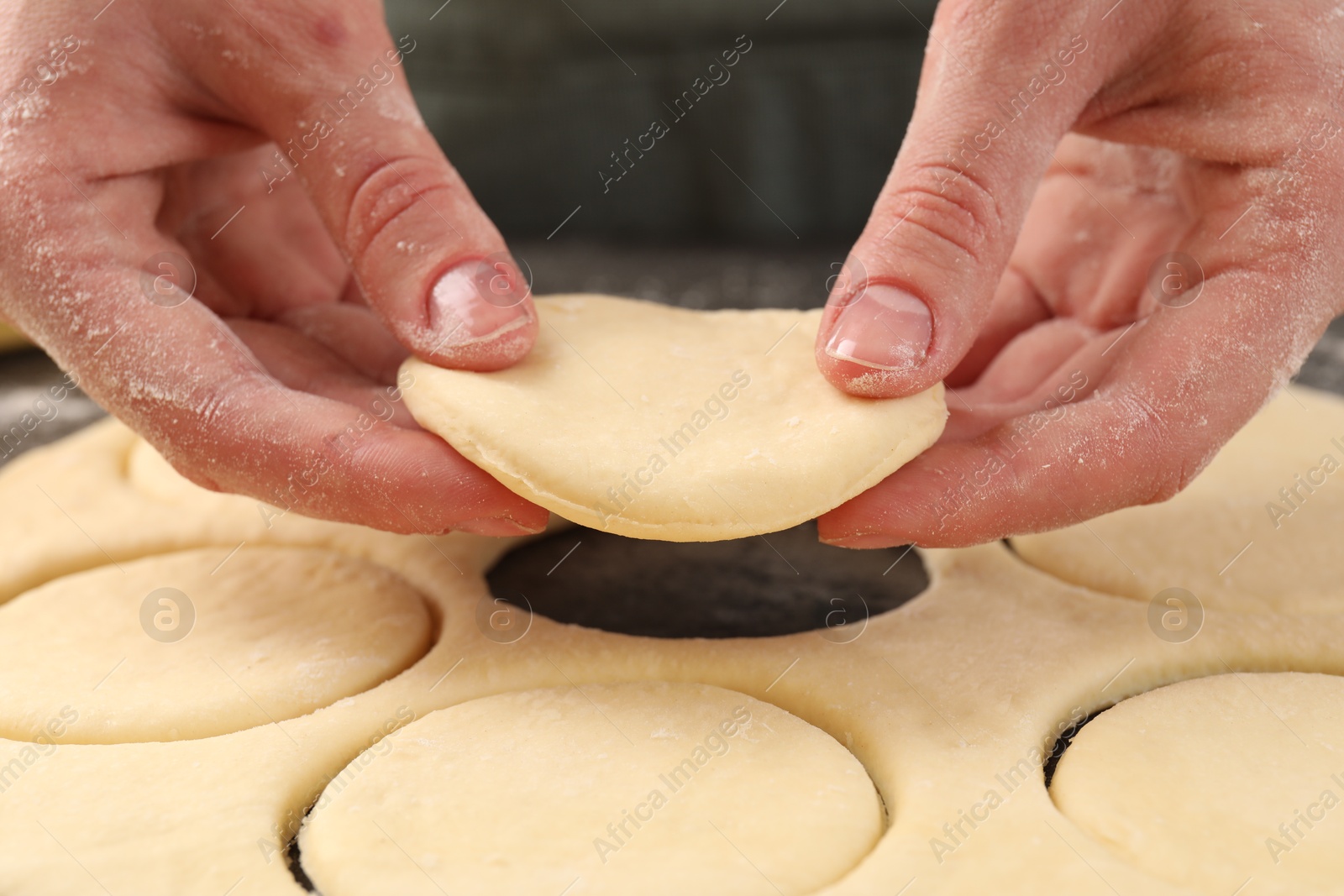 Photo of Woman making pirozhki (stuffed pastry pies) at table, closeup