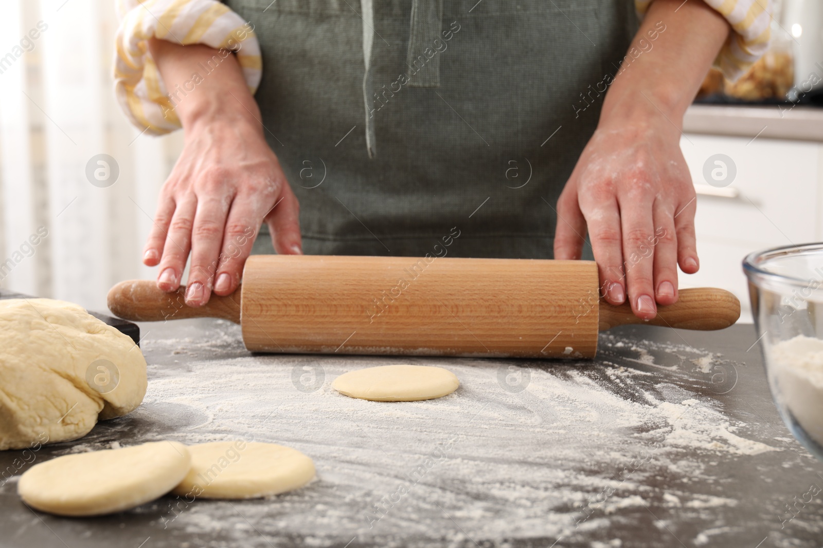 Photo of Making pirozhki (stuffed pastry pies). Woman shaping dough with rolling pin at gray table, closeup