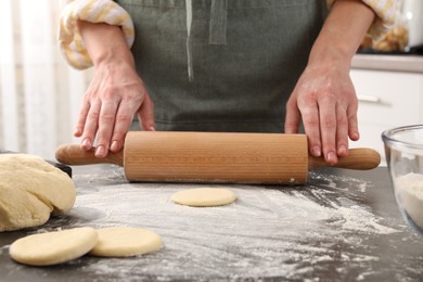 Photo of Making pirozhki (stuffed pastry pies). Woman shaping dough with rolling pin at gray table, closeup