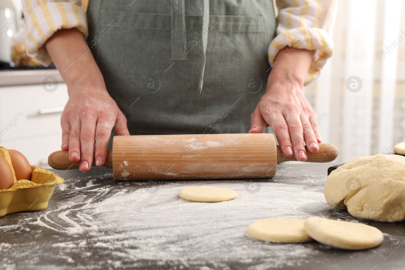 Photo of Making pirozhki (stuffed pastry pies). Woman shaping dough with rolling pin at gray table, closeup