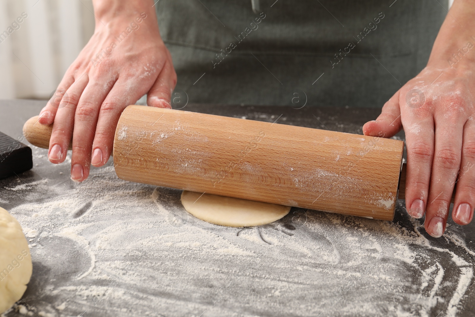 Photo of Making pirozhki (stuffed pastry pies). Woman shaping dough with rolling pin at gray table, closeup