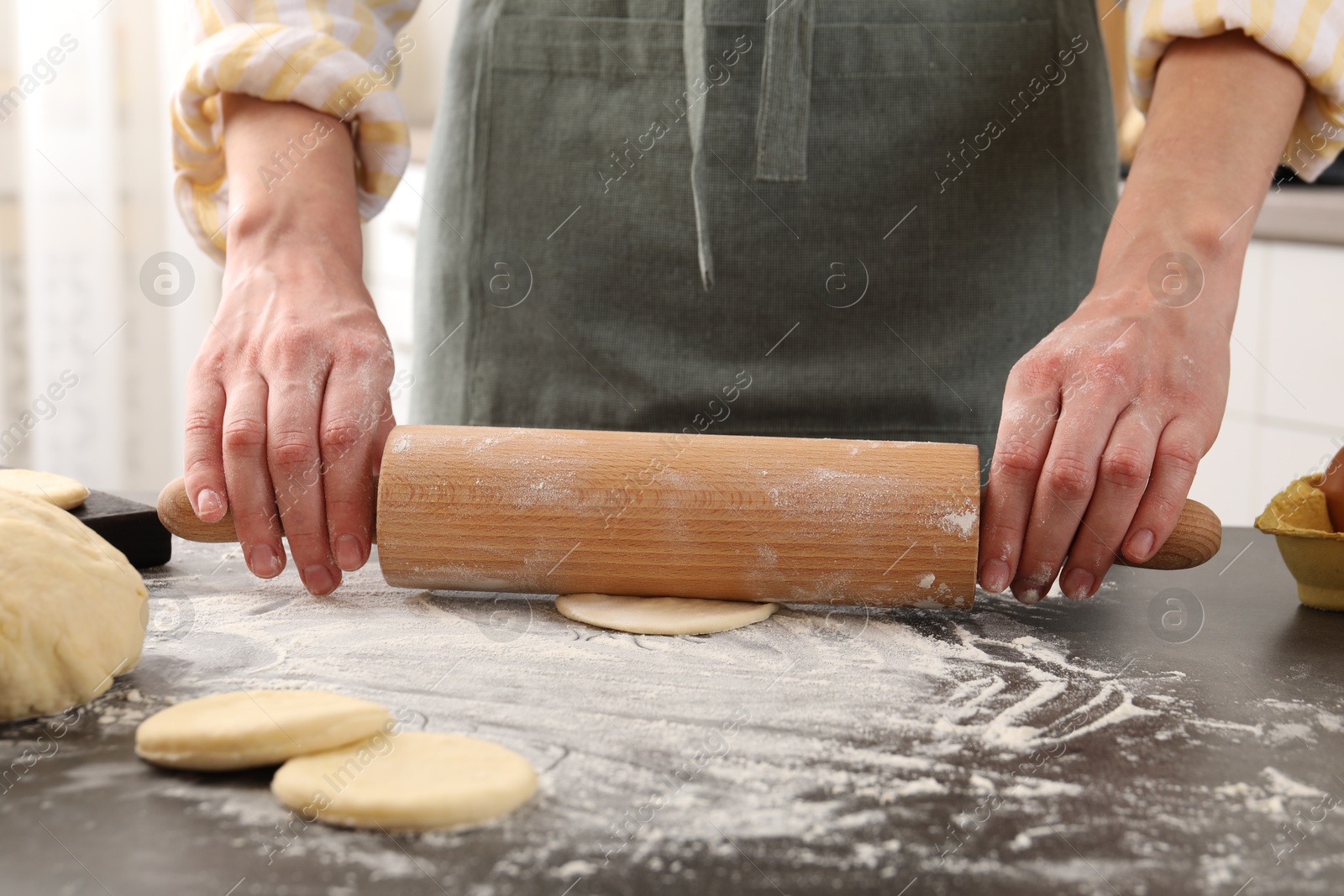 Photo of Making pirozhki (stuffed pastry pies). Woman shaping dough with rolling pin at gray table, closeup