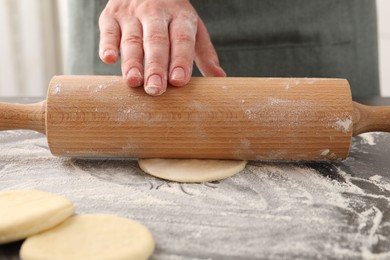 Photo of Making pirozhki (stuffed pastry pies). Woman shaping dough with rolling pin at gray table, closeup