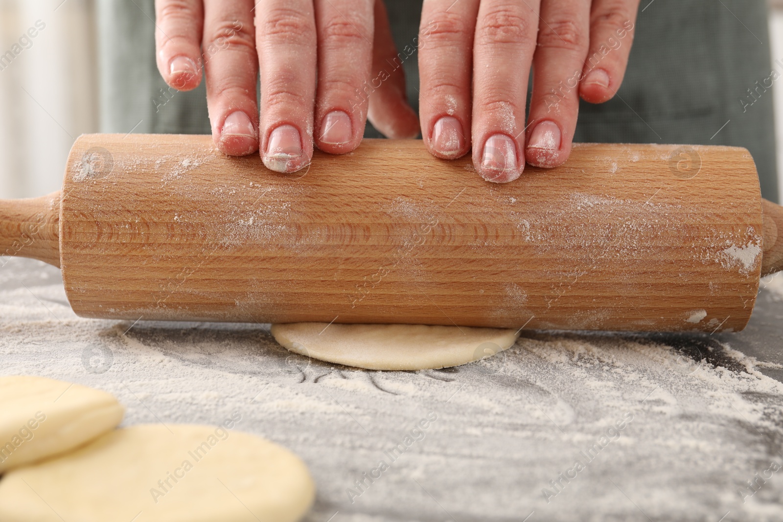 Photo of Making pirozhki (stuffed pastry pies). Woman shaping dough with rolling pin at table, closeup