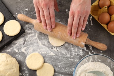 Photo of Making pirozhki (stuffed pastry pies). Woman shaping dough with rolling pin at gray table, top view