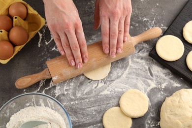 Photo of Making pirozhki (stuffed pastry pies). Woman shaping dough with rolling pin at gray table, top view