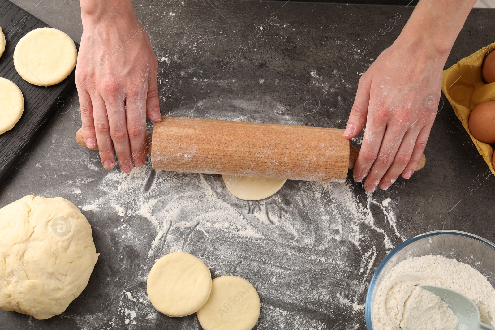 Photo of Making pirozhki (stuffed pastry pies). Woman shaping dough with rolling pin at gray table, top view