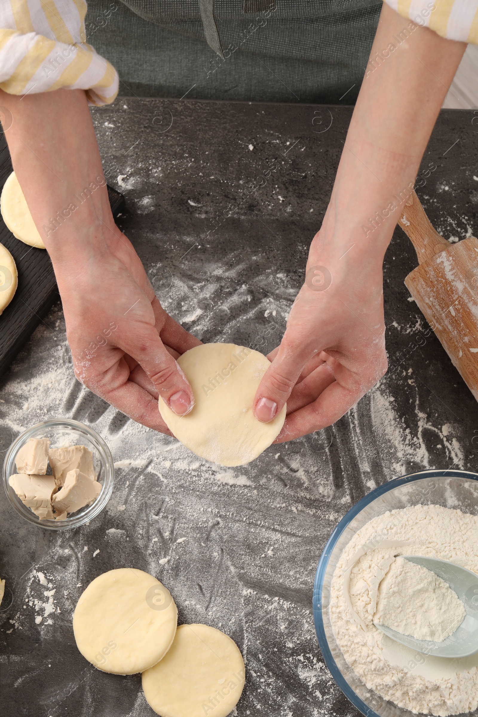 Photo of Woman making pirozhki (stuffed pastry pies) at gray table, above view