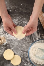 Photo of Woman making pirozhki (stuffed pastry pies) at gray table, top view