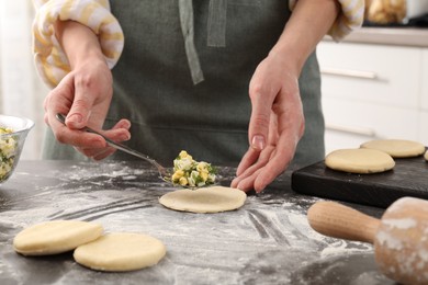 Photo of Woman making pirozhki (stuffed pastry pies) with eggs and dill at gray table indoors, closeup