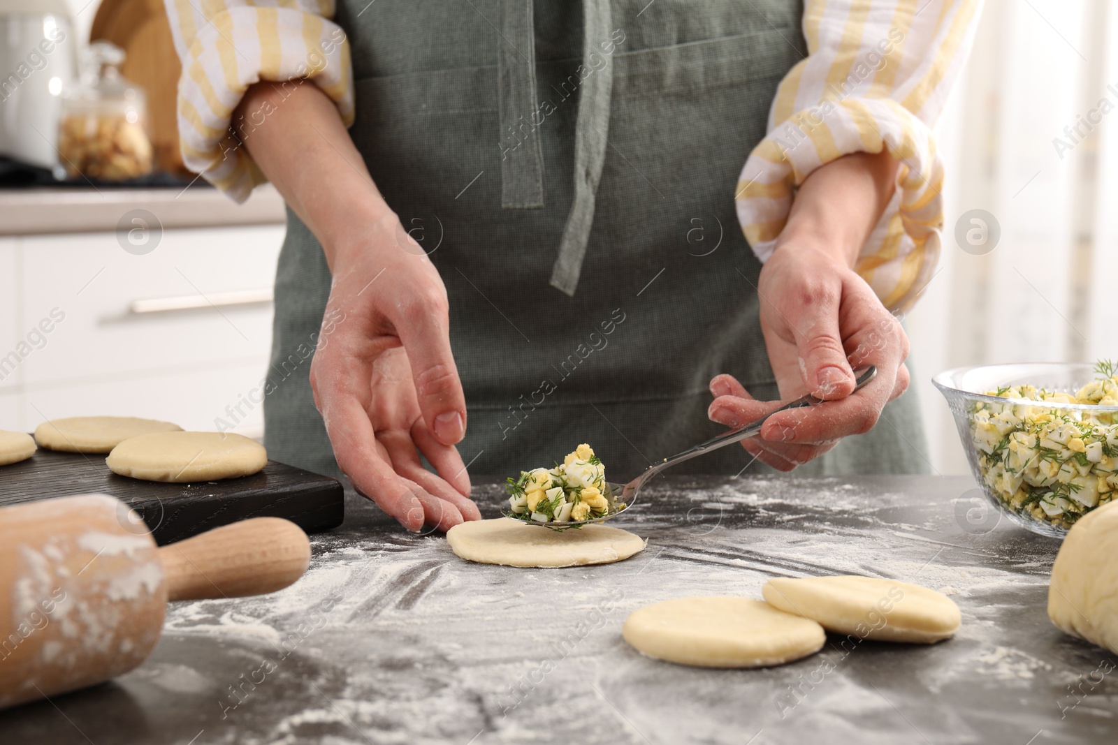 Photo of Woman making pirozhki (stuffed pastry pies) with eggs and dill at gray table indoors, closeup