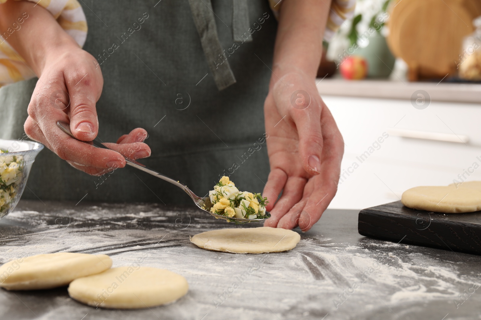 Photo of Woman making pirozhki (stuffed pastry pies) with eggs and dill at gray table indoors, closeup