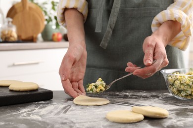 Photo of Woman making pirozhki (stuffed pastry pies) with eggs and dill at gray table indoors, closeup