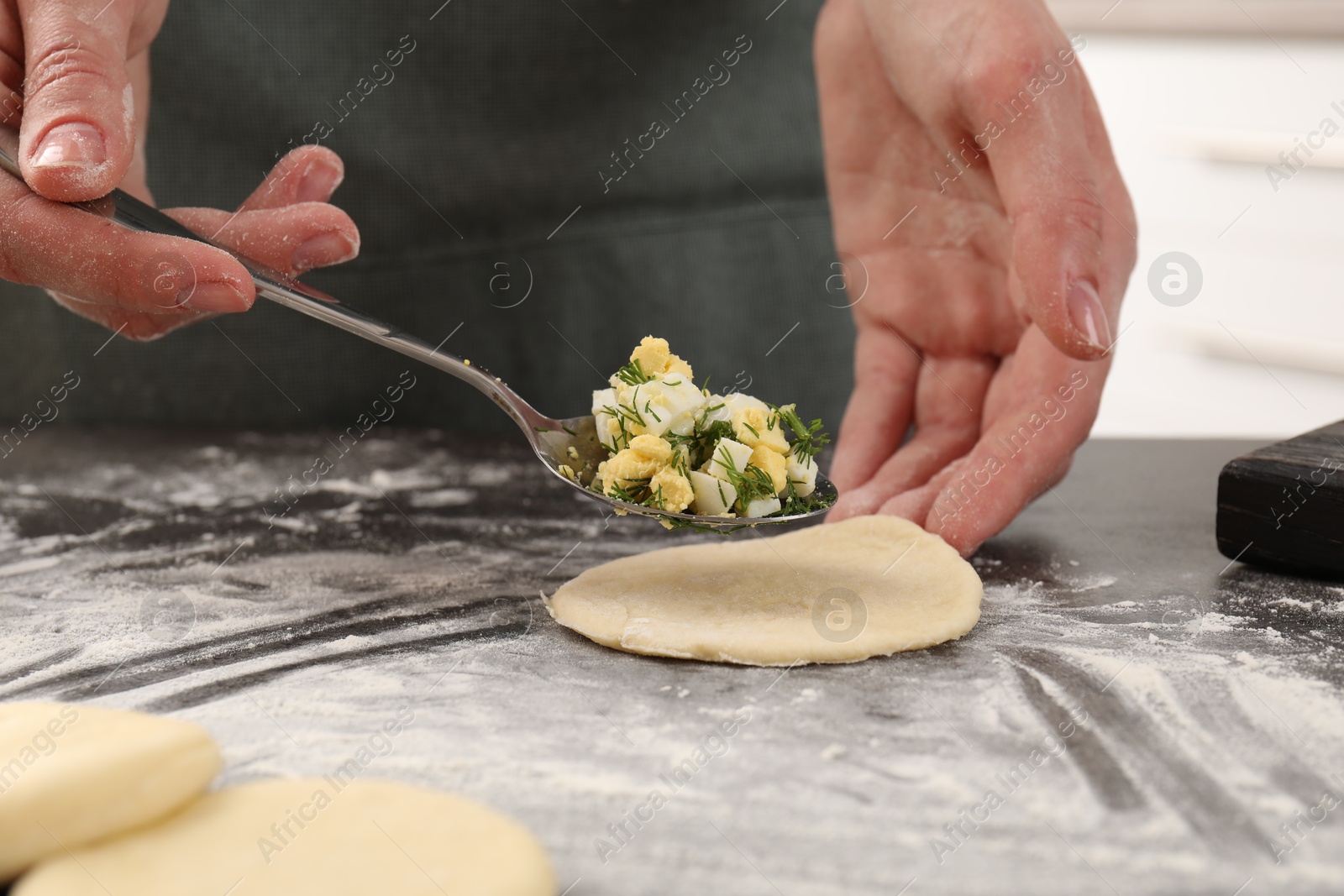 Photo of Woman making pirozhki (stuffed pastry pies) with eggs and dill at gray table indoors, closeup