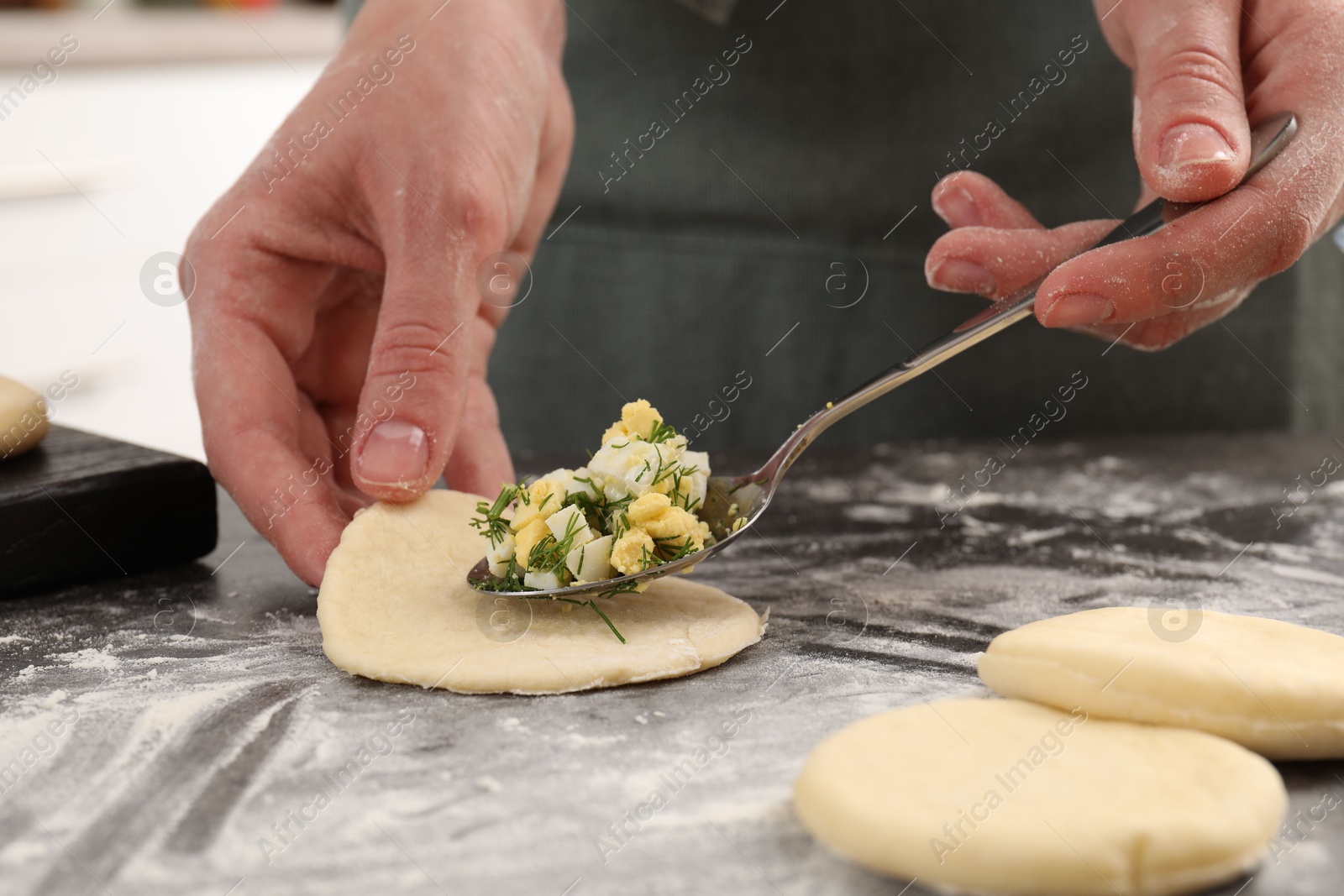 Photo of Woman making pirozhki (stuffed pastry pies) with eggs and dill at gray table indoors, closeup