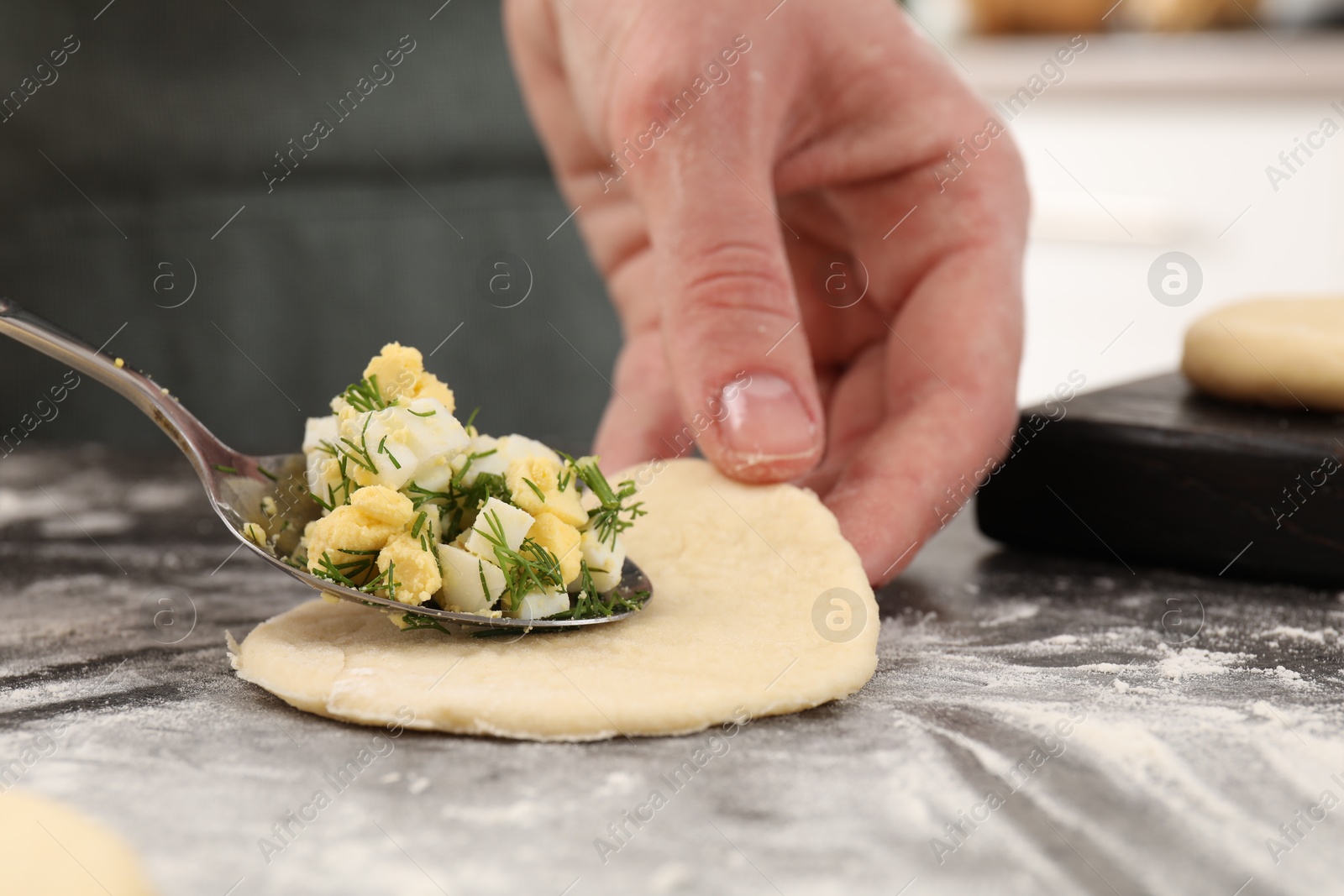 Photo of Woman making pirozhki (stuffed pastry pies) with eggs and dill at gray table indoors, closeup