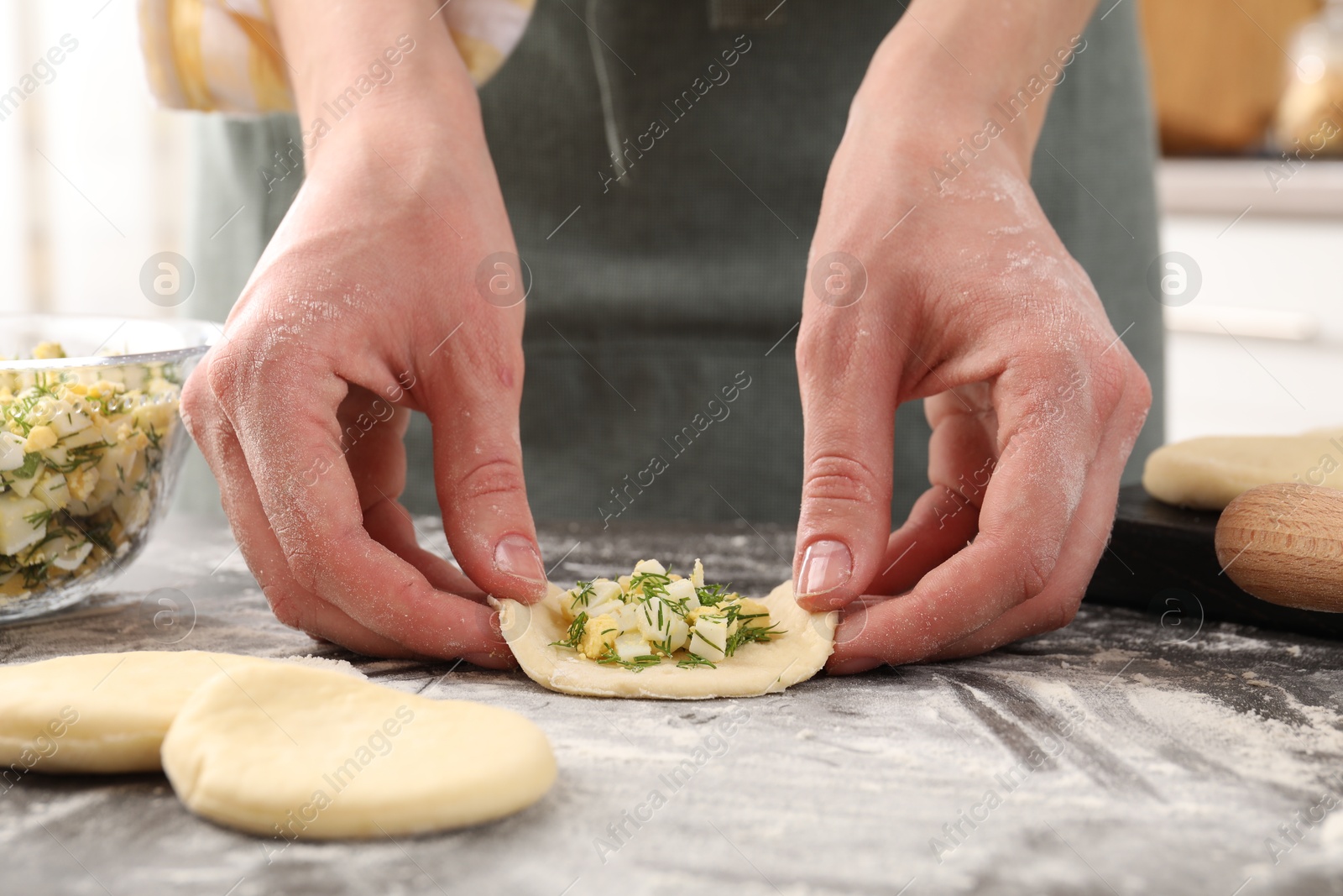 Photo of Woman making pirozhki (stuffed pastry pies) with eggs and dill at gray table indoors, closeup