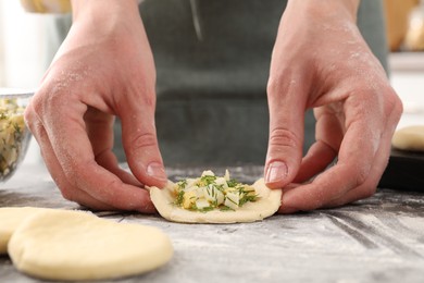 Photo of Woman making pirozhki (stuffed pastry pies) with eggs and dill at gray table indoors, closeup