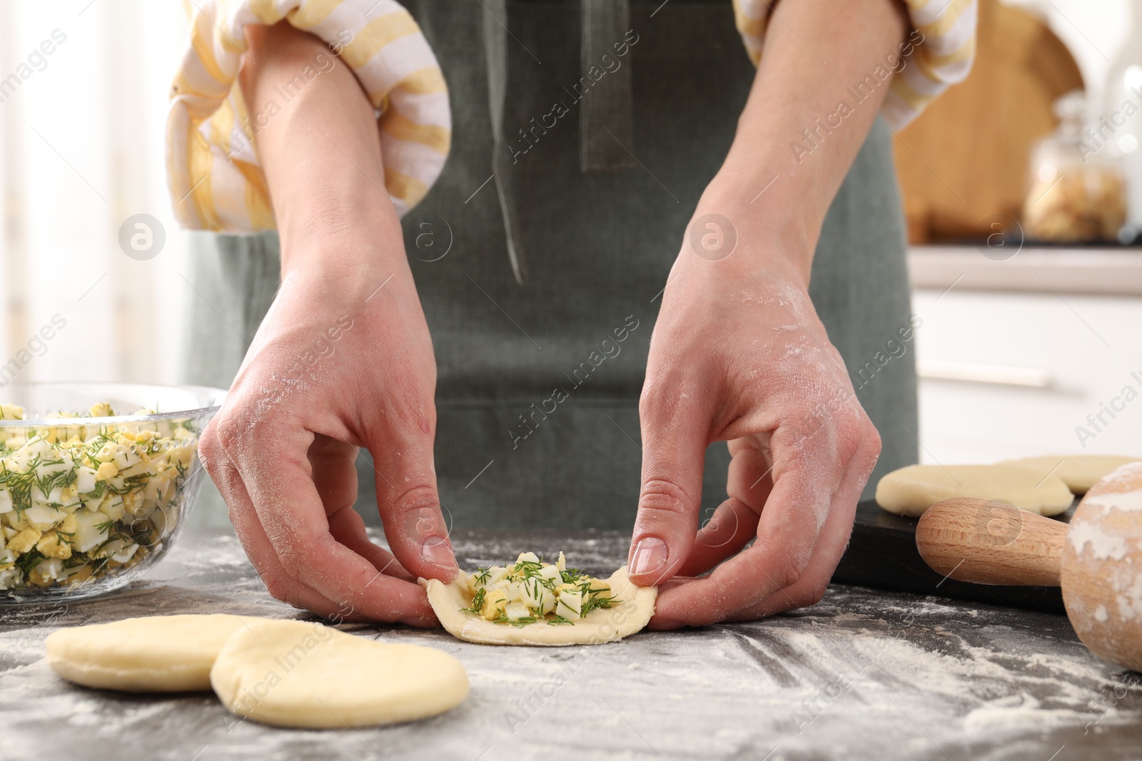 Photo of Woman making pirozhki (stuffed pastry pies) with eggs and dill at gray table indoors, closeup