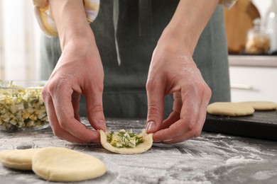 Photo of Woman making pirozhki (stuffed pastry pies) with eggs and dill at gray table indoors, closeup