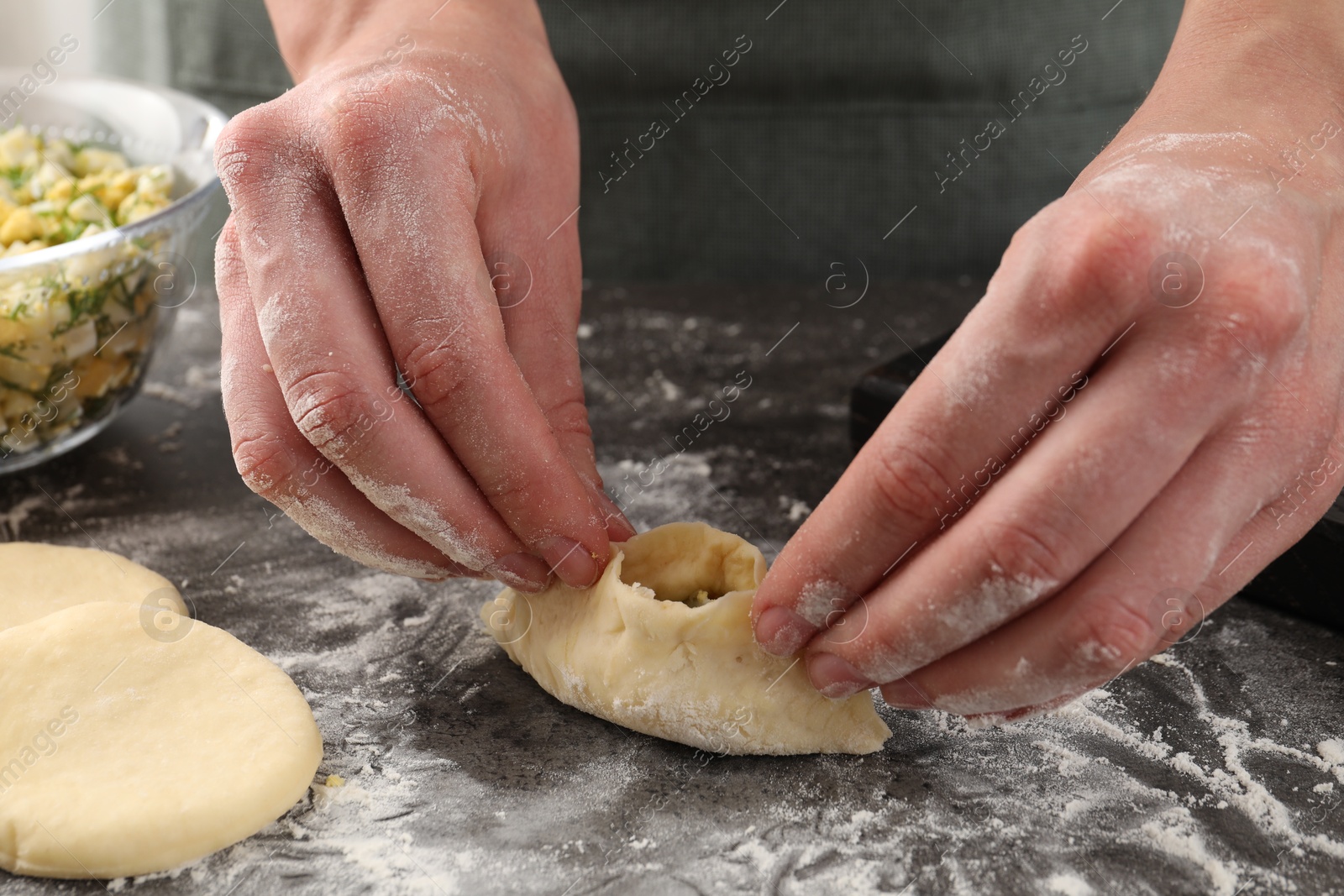 Photo of Woman making pirozhki (stuffed pastry pies) with eggs and dill at gray table indoors, closeup