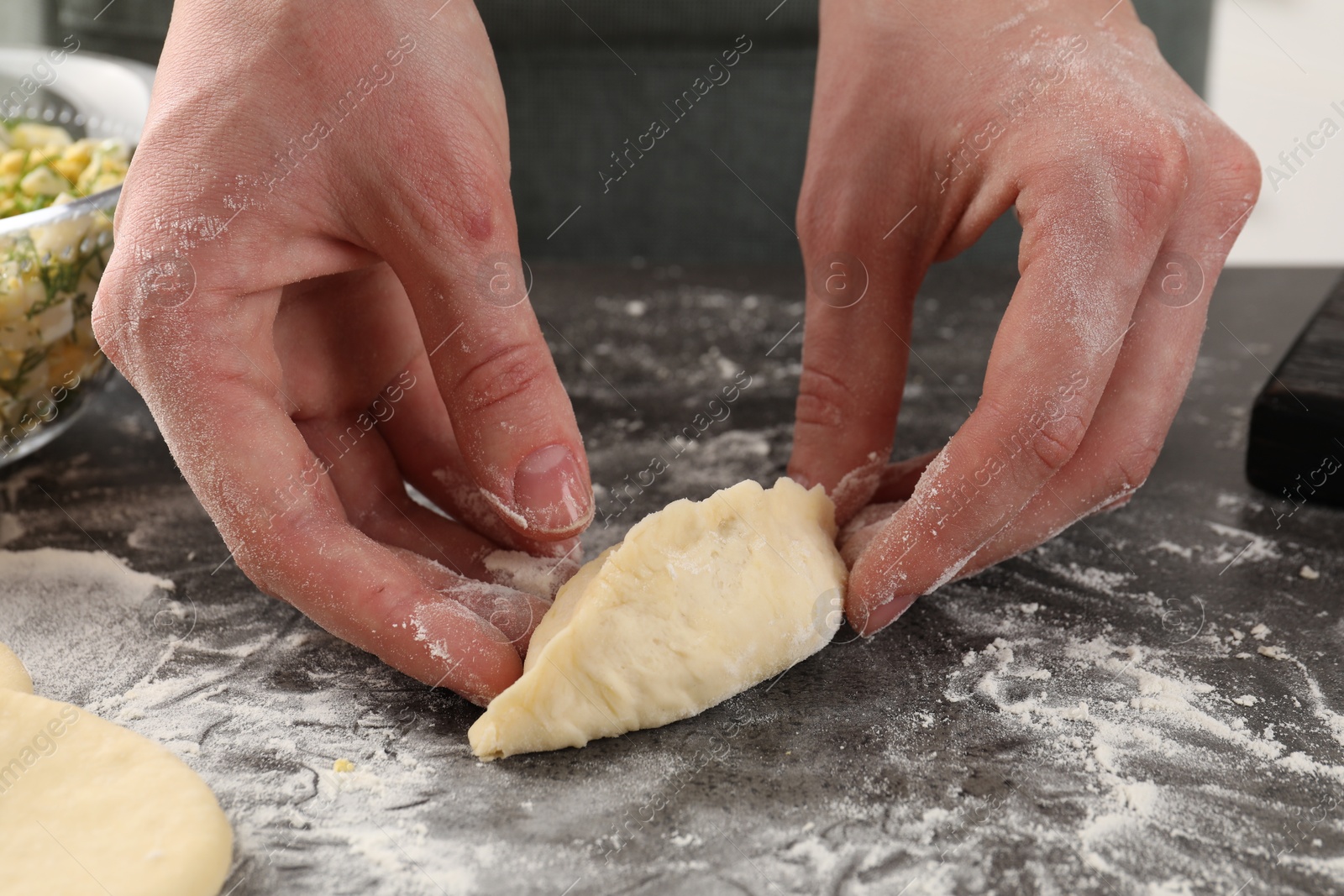 Photo of Woman making pirozhki (stuffed pastry pies) with eggs and dill at gray table indoors, closeup