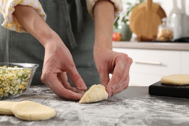 Photo of Woman making pirozhki (stuffed pastry pies) with eggs and dill at gray table indoors, closeup