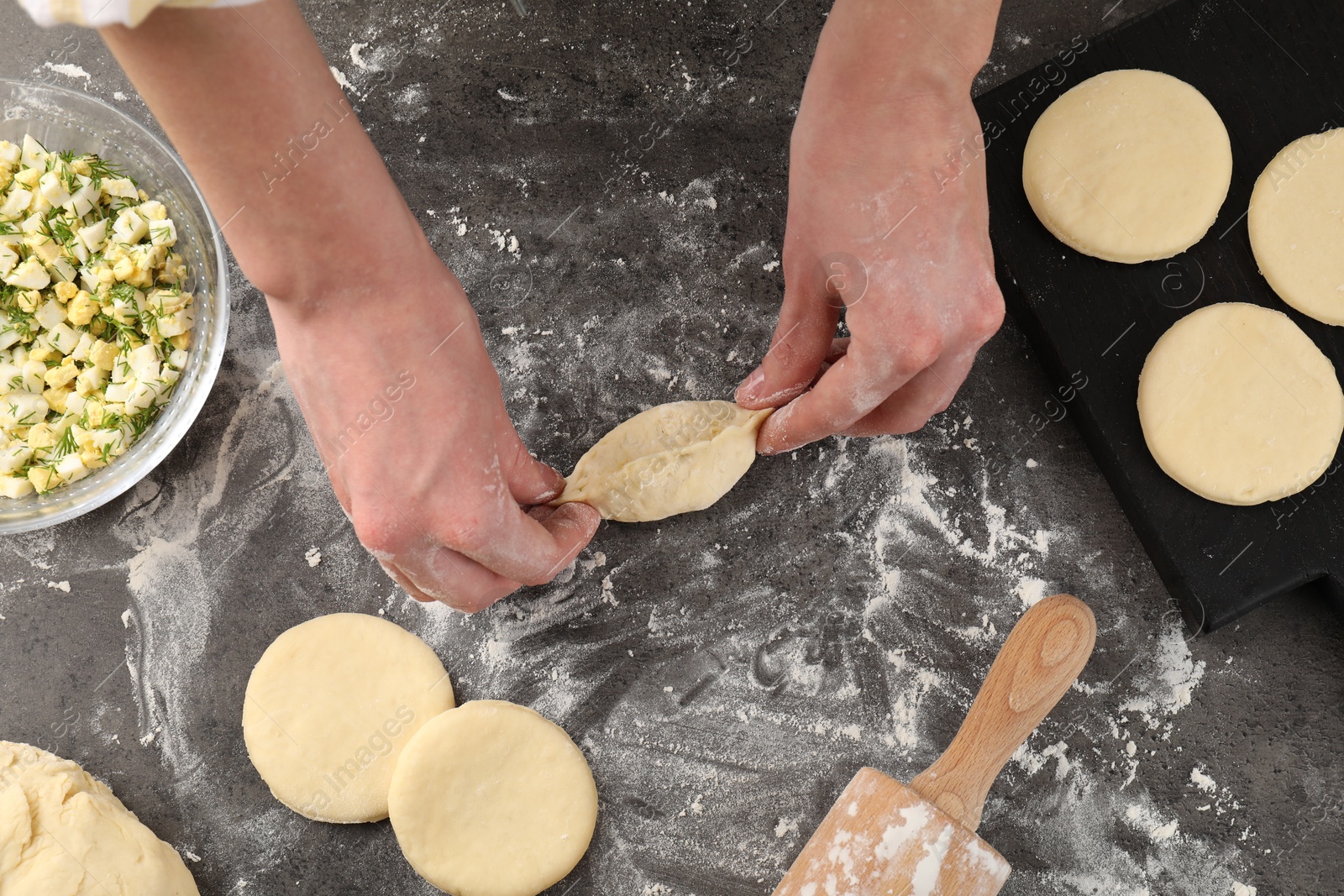 Photo of Woman making pirozhki (stuffed pastry pies) at gray table, top view