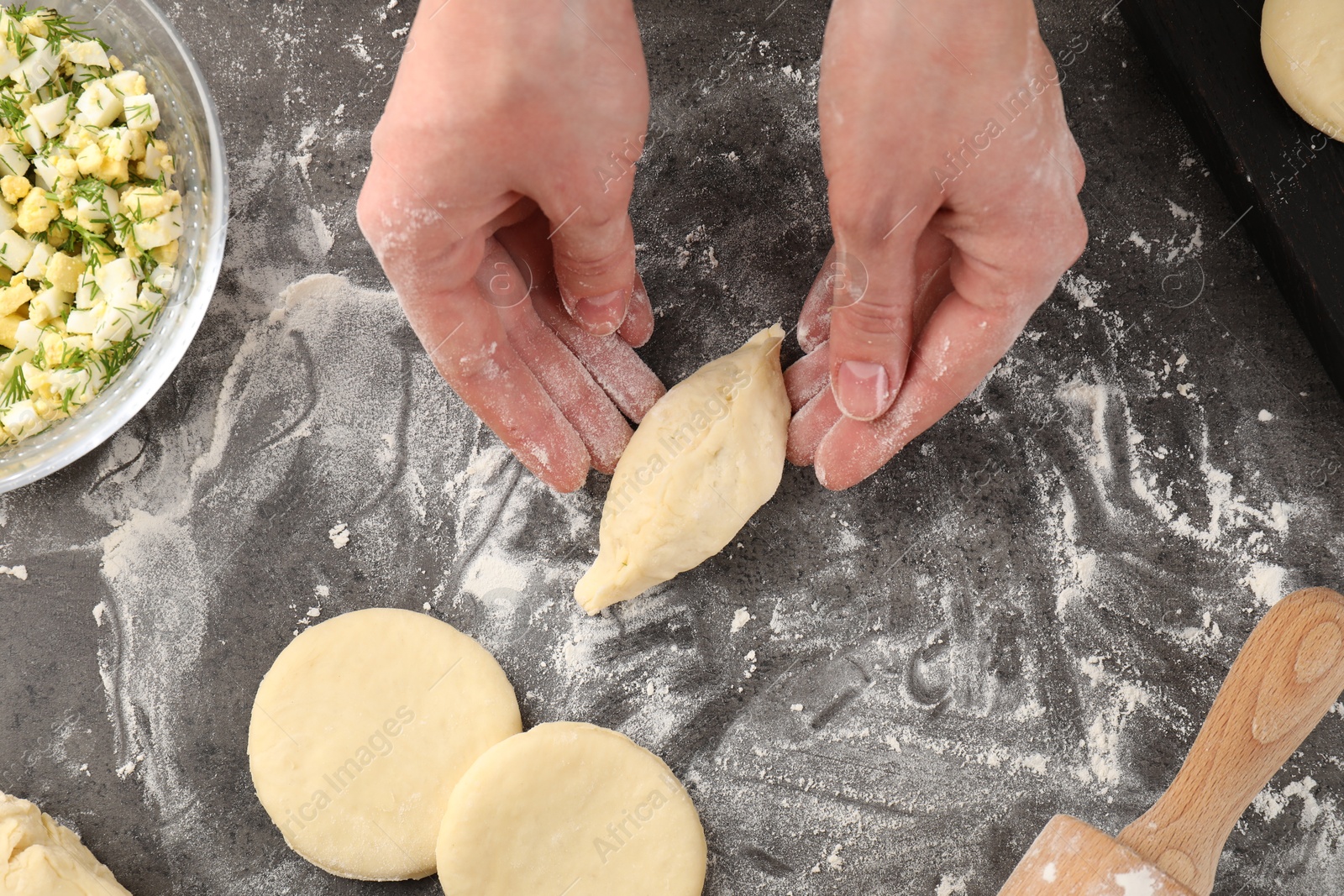 Photo of Woman making pirozhki (stuffed pastry pies) at gray table, top view