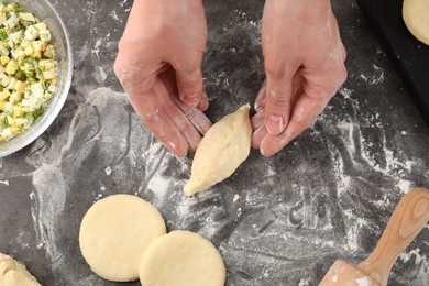 Photo of Woman making pirozhki (stuffed pastry pies) at gray table, top view