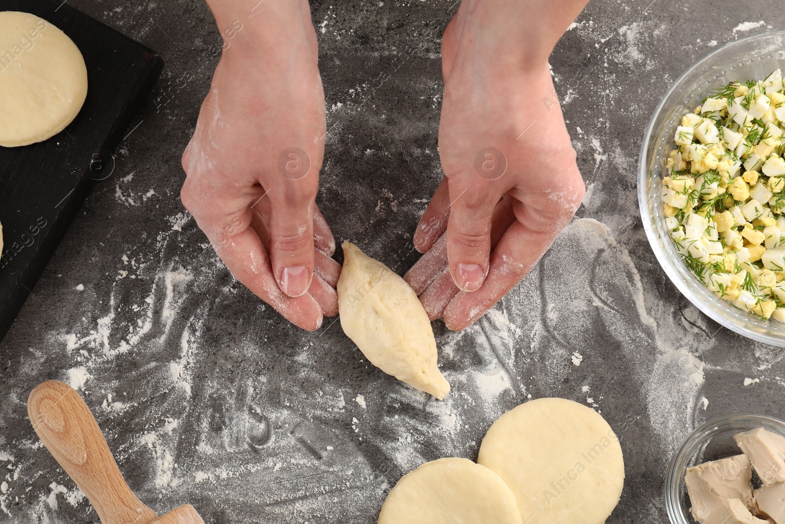 Photo of Woman making pirozhki (stuffed pastry pies) at gray table, top view